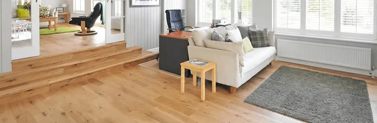 A modern living room with professionally installed laminate flooring, a beige sofa, a small side table, a gray rug, and large windows with white shutters in Arvada, CO